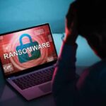 Person distressed over ransomware screen on laptop.