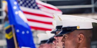 Marines in uniform standing in line, American flags displayed.