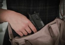 Hand placing handgun into beige handbag.