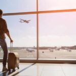 Avoid Falling Victim: Top Travel Scams Every Tourist Should Know In 2024 Traveler with luggage watches airplane take off at airport.