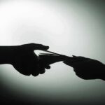 Uncovering Alleged Chinese Communist Involvement with US Police Foundation Silhouette of hands exchanging money in dim light.