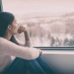 Reviving Tradition: How Stammtisch Meetings Foster Real Connections Today Woman sitting by window looking outside snowy landscape