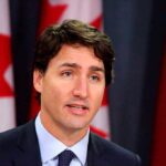 Trudeau Faces Turmoil: Cabinet Disputes and Mounting Resignation Pressure Man speaking in front of Canadian flags.