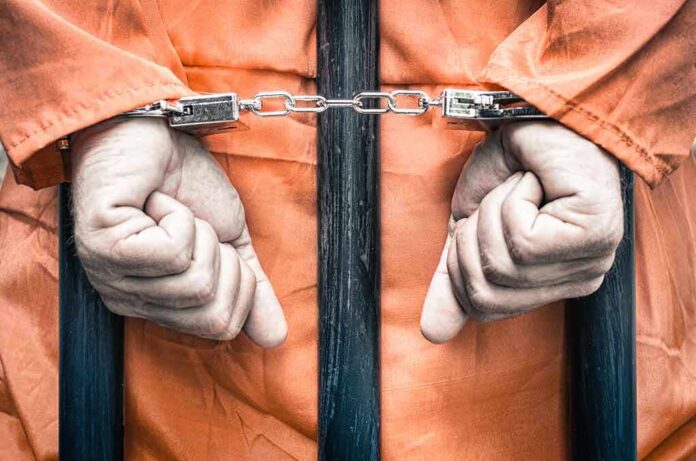 217094626 featured image Handcuffed hands in orange jumpsuit behind bars.