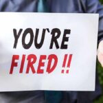 Person holding YOU'RE FIRED sign.