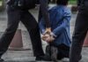 Person handcuffed by police officers on street kneeling