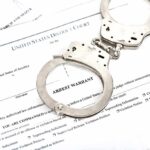 Handcuffs on top of an arrest warrant document