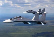 Two fighter jets flying in formation over green landscape.