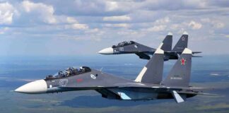 Two fighter jets flying in formation over green landscape.