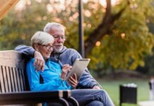 Older couple sitting on bench using tablet outdoors