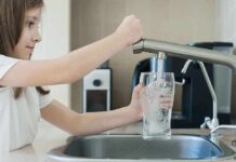 Girl filling glass with water from kitchen faucet.