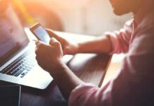 Person using smartphone and laptop at desk