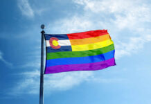 Colorful flag with rainbow stripes against blue sky