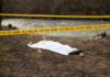 Crime scene with body near river and police tape