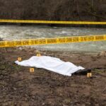 Crime scene with body near river and police tape