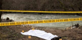 Crime scene with body near river and police tape
