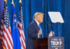 Person speaking at podium with flags in background