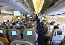 Interior view of an airplane with passengers seated and using in flight entertainment screens