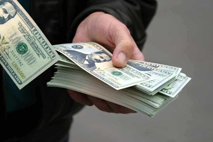 shutterstock_2908150.jpg A hand holding a stack of hundred dollar bills with one bill prominently displayed