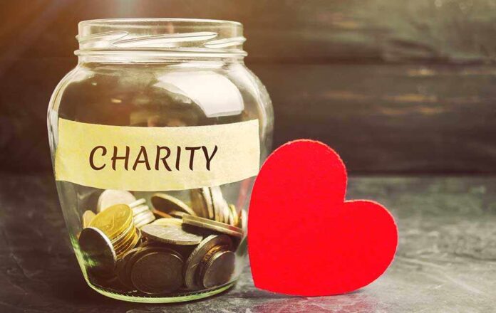 A glass jar labeled CHARITY filled with coins next to a red heart shape