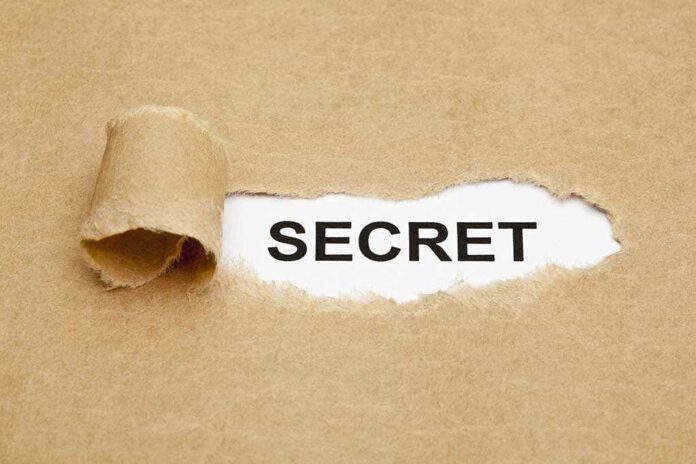 shutterstock_147112922.jpg A torn piece of brown paper revealing the word SECRET underneath