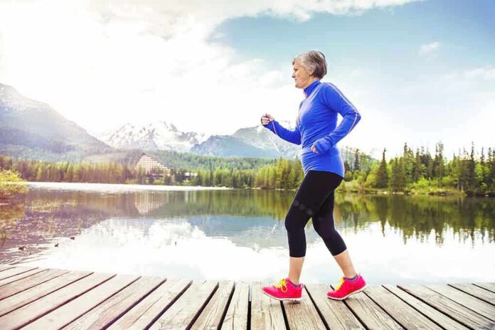 Senior woman jogging along a lakeside with mountains in the background
