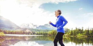 Senior woman jogging along a lakeside with mountains in the background