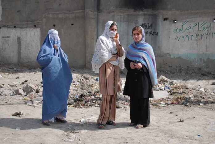 Three women in traditional attire standing in an urban setting with debris in the background