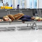 Shocking Drone Evasion—Airports Close AGAIN! A traveler sleeping on a bench in an airport waiting area