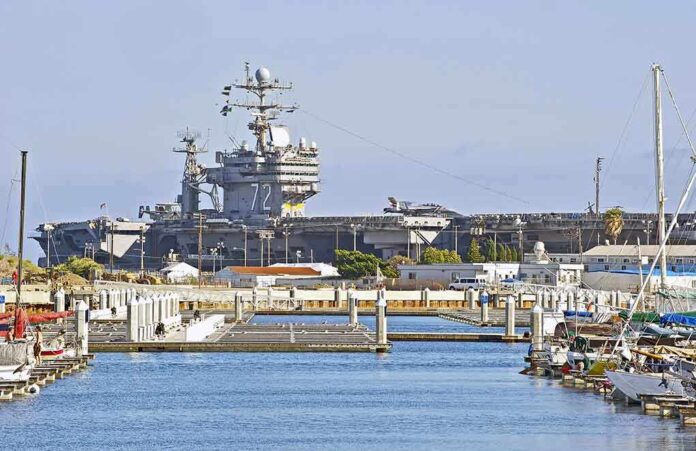 shutterstock_194774165.jpg A large naval aircraft carrier docked in a harbor with smaller boats in the foreground