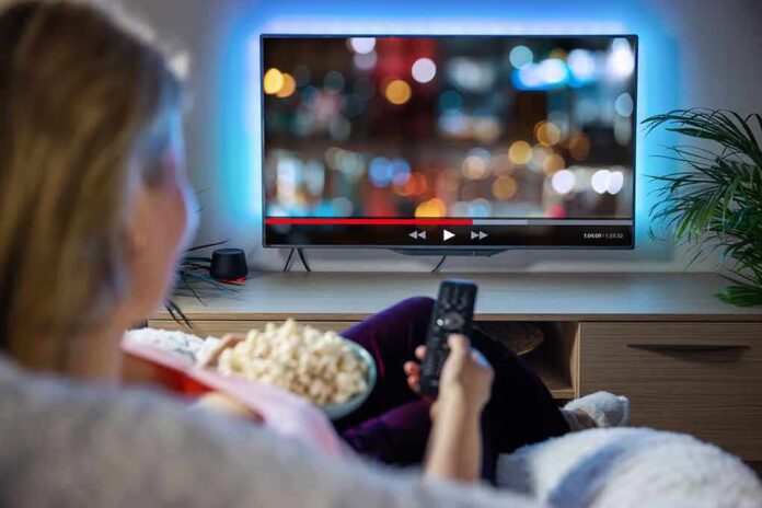 Person sitting on a couch watching a movie on a TV with popcorn in hand