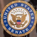 Official seal of the United States Senate with microphones in the background