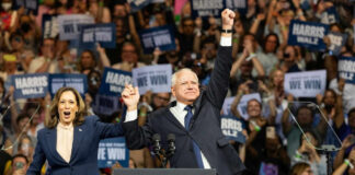 Two people celebrate on stage with supporters behind.