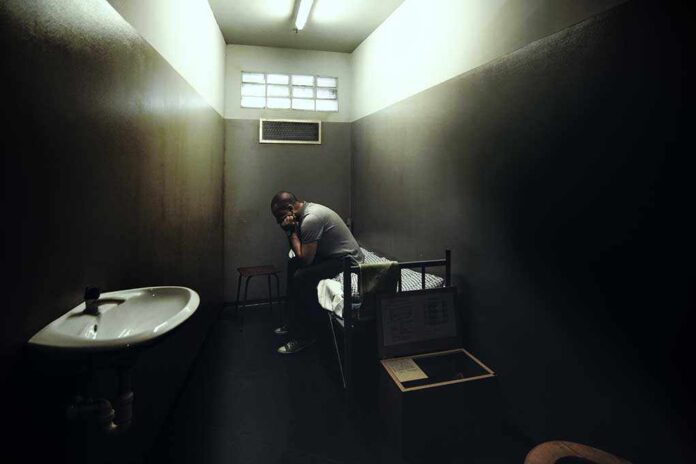 A person sitting in a dimly lit prison cell, appearing contemplative and distressed