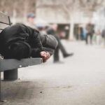Socialist Mayor Tells Cops: “Stand Down!” Person sleeping on a bench in a public area.