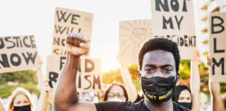 Protester raises fist, wears mask, signs in background.