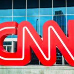Explosive CNN Clash – Noem EMBARRASSES Host on Air Large red CNN logo in front of a glass building