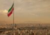 Iran’s Grip Cracks – 544 Protestors Dead! Iranian flag waving over a city skyline with mountains in the background