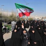 Group of women in black attire marching with an Iranian flag