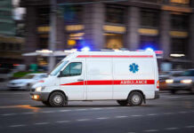 Ambulance driving on urban street with lights flashing.