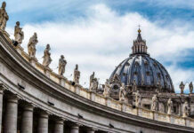 St. Peters Basilica dome with statues and clouds.