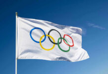 Olympic flag waving against clear blue sky.