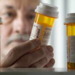 Big Pharma Price Wall Cracks An elderly man holding a prescription bottle while examining it closely