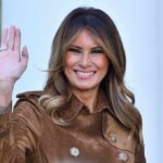 Melania Trump waving and smiling while wearing a stylish coat