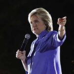 A woman speaking into a microphone while gesturing with her hand