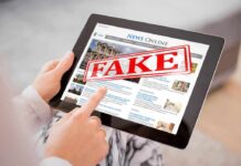 Person holding a tablet displaying a news website with a 'FAKE' stamp