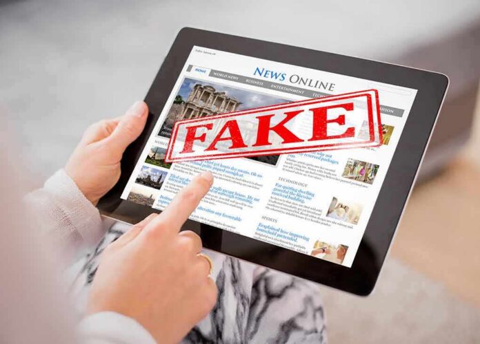 shutterstock_675861955 (1).jpg Person holding a tablet displaying a news website with a 'FAKE' stamp