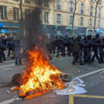 Protesters and police clash; fire in the street.