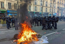 Protesters and police clash; fire in the street.