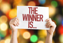 Hands holding a sign reading The Winner Is